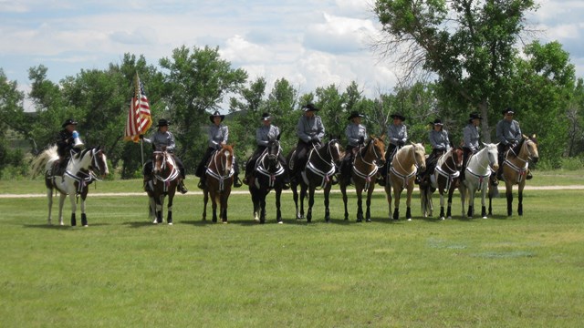 Image of people on horses, holding the America flag, standing in a line. 