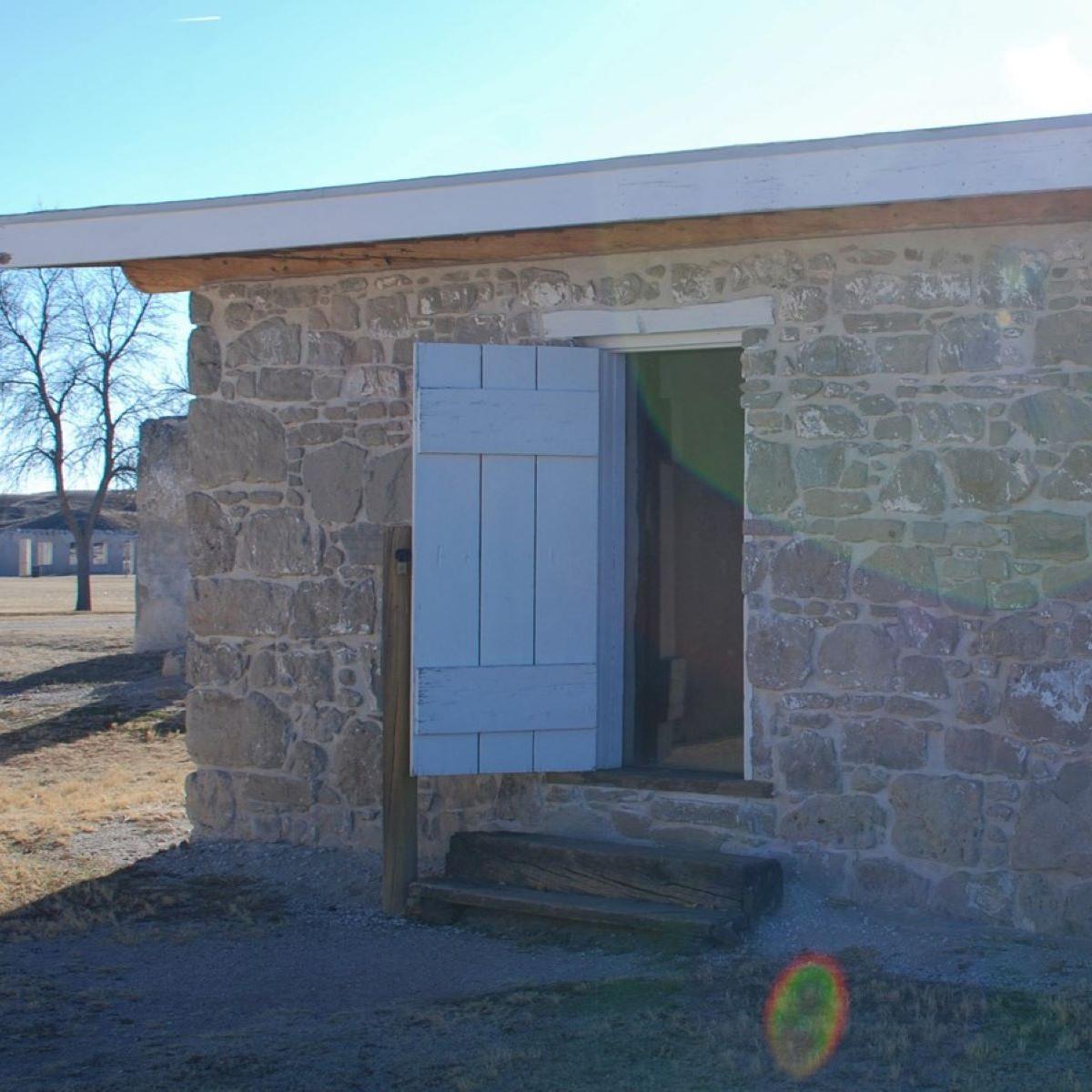 A small brown stone building with a white roof and one small door. 