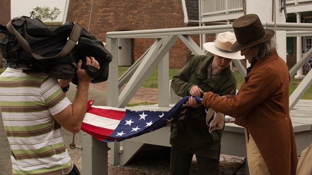 A man with a camera filming a ranger with a flag.