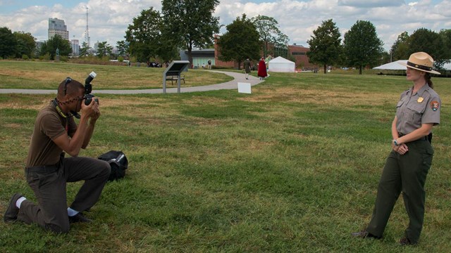 A man on his knee taking a photo of a park ranger.