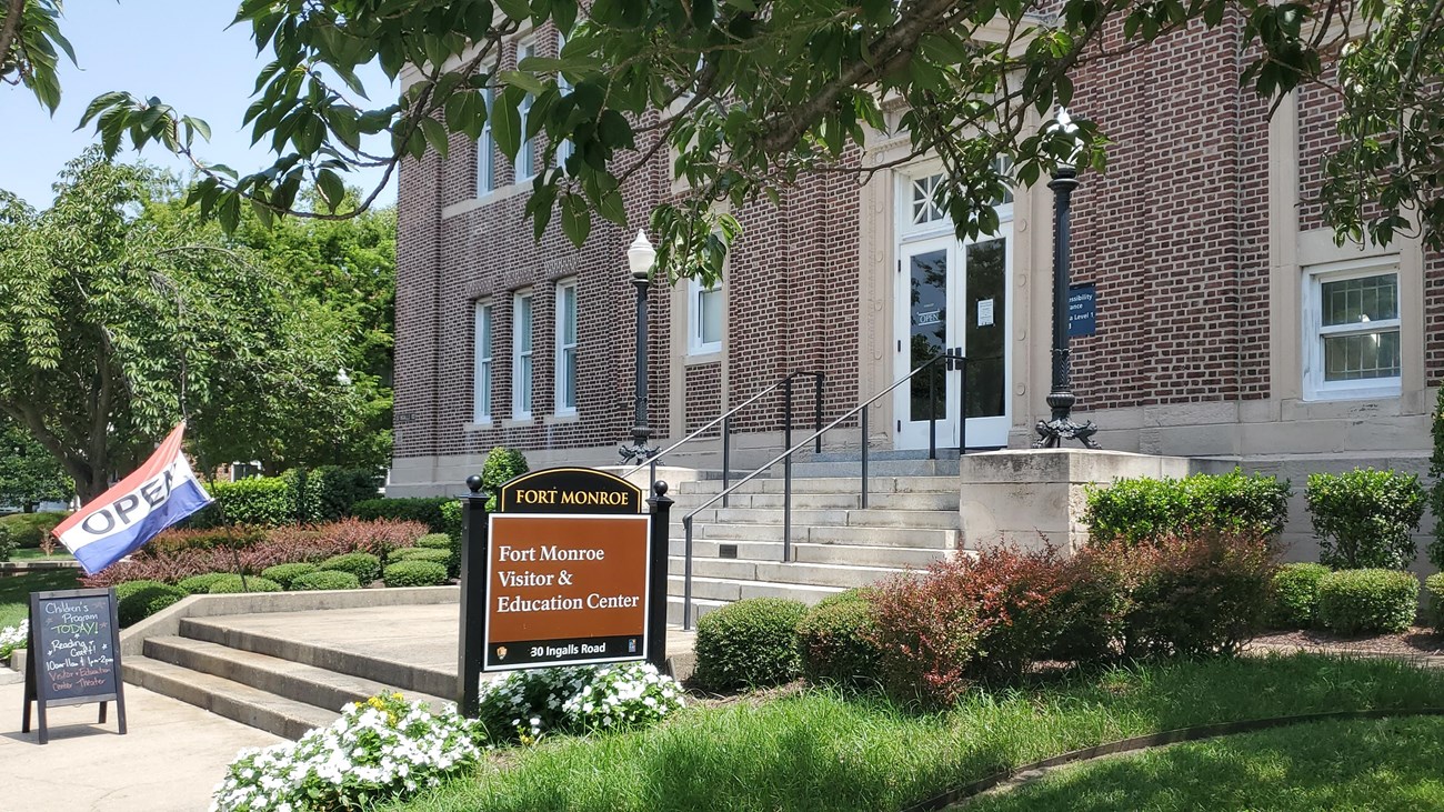 Signs in front of a brick Beaux-Arts style building state that the visitor center is open.