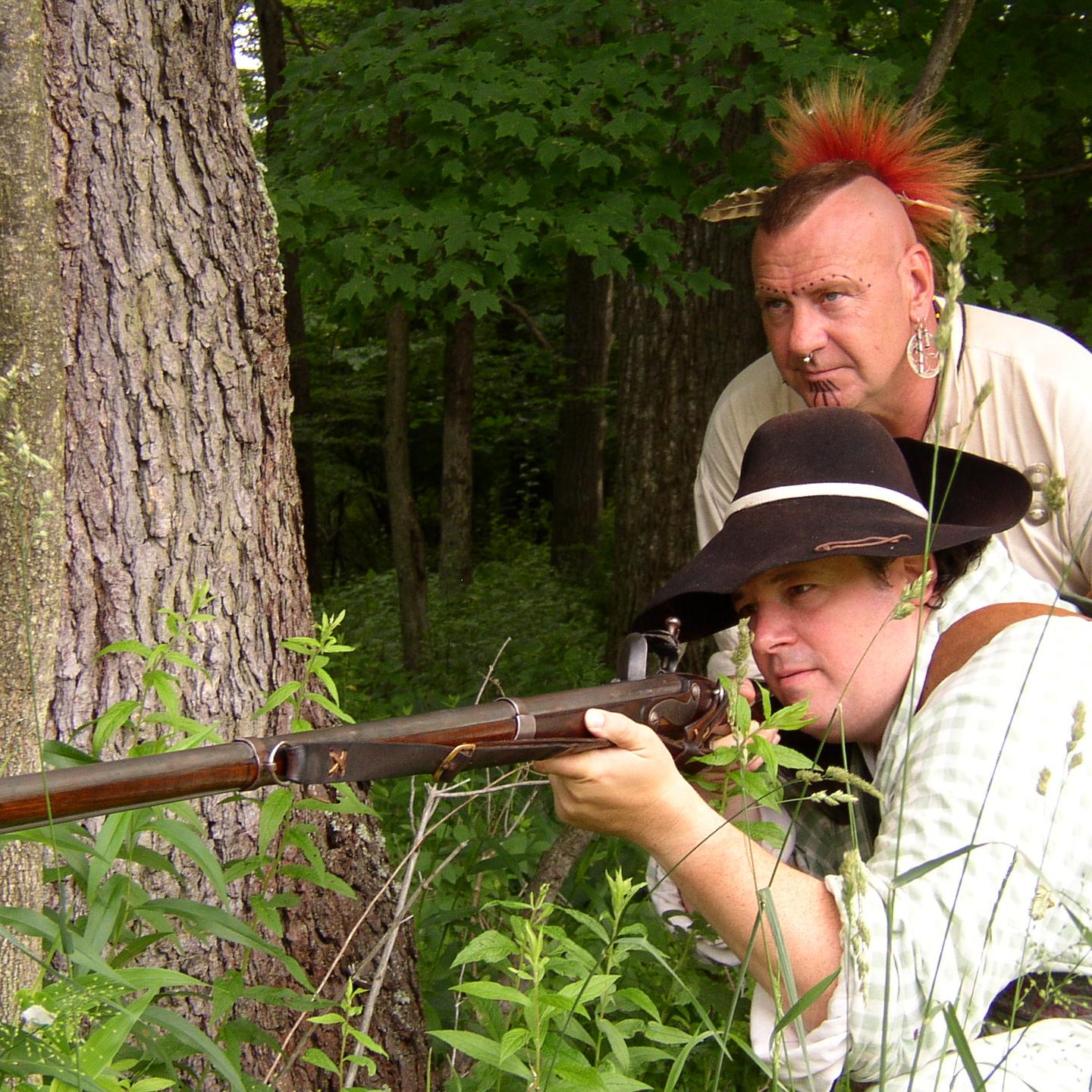 Settler and American Indian peering from behind a tree