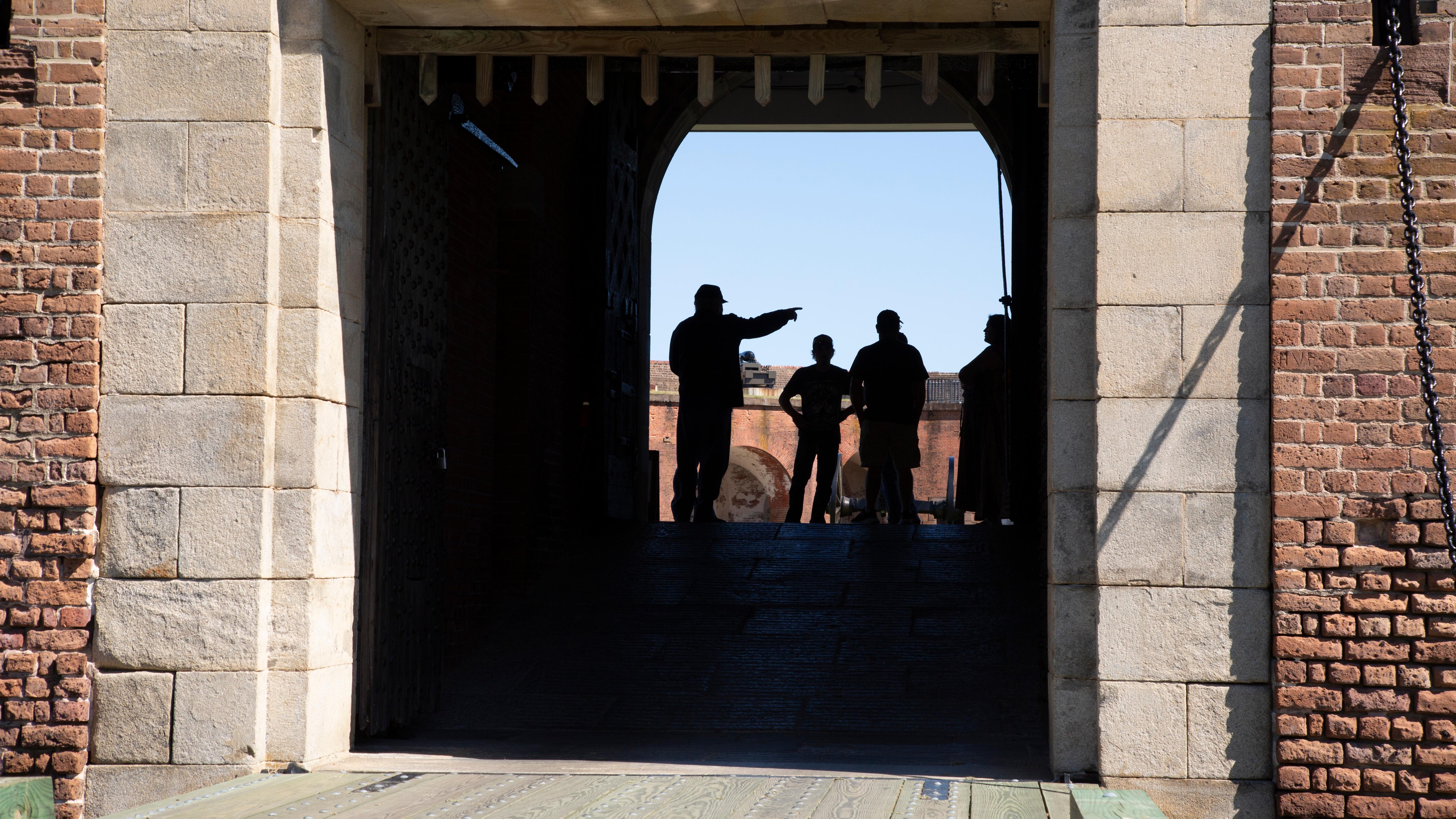 A man in period clothing pointing something out to a group of 3 people, seen through a large doorway