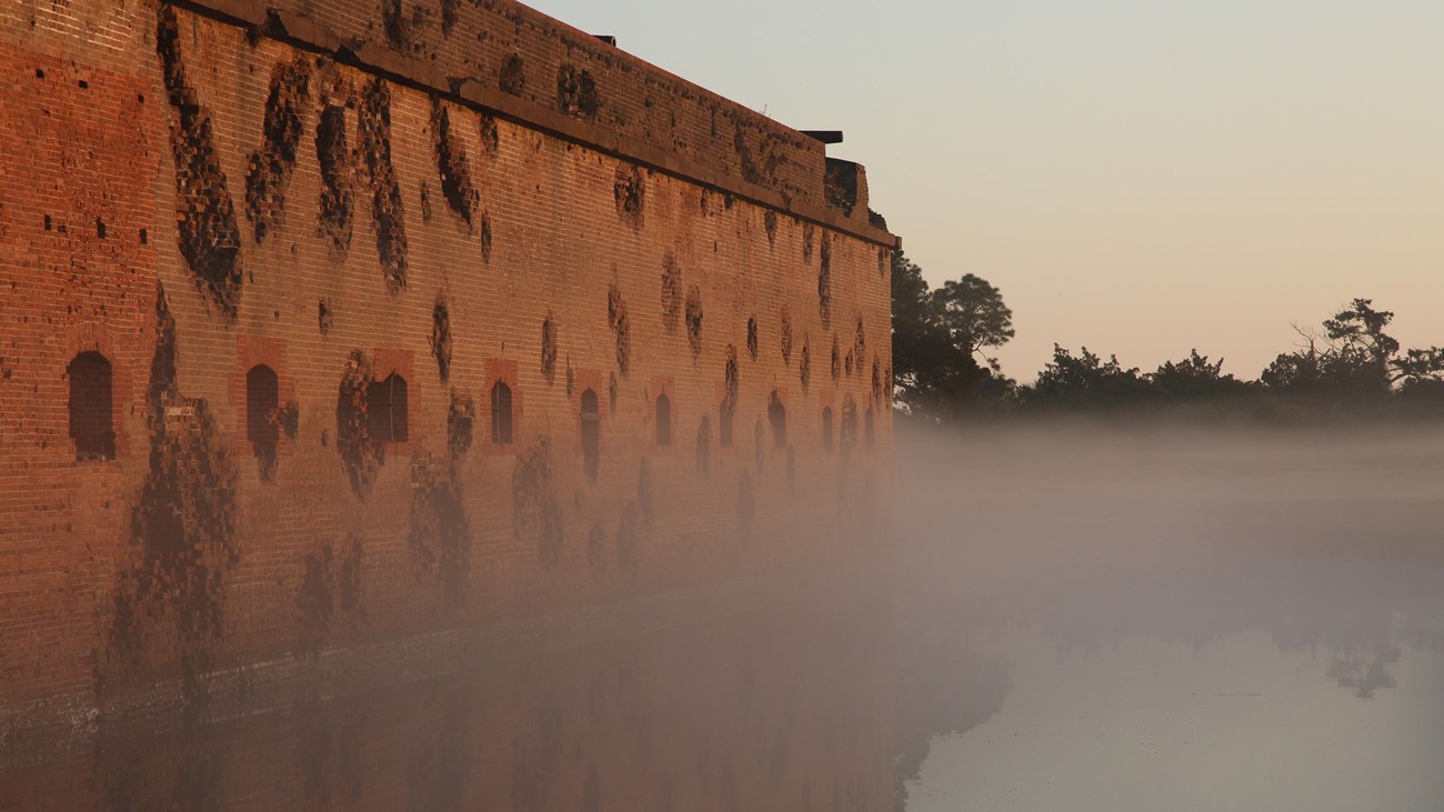 Foggy sunrise with a brick fort reflected in a moat. 