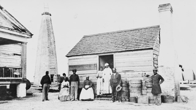 a black and white image of a cabin and a group of people in front
