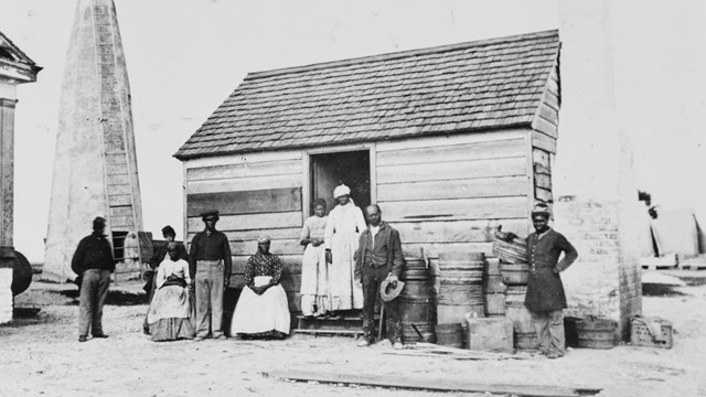 Black and white photograph of freedpeople in front of a house on Cockspur Island.