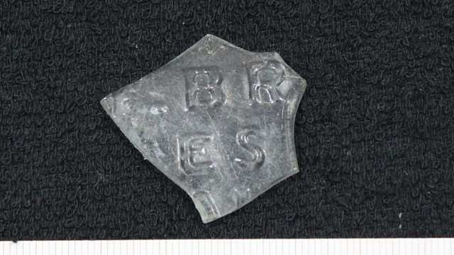 colorless glass bottle fragment with letter embossed on it. 