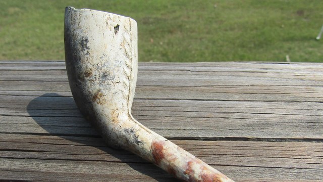 Nearly complete white clay tobacco pipe sitting on a wood plank.
