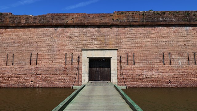 A large brick building with a drawbridge and a closed wooden door. 