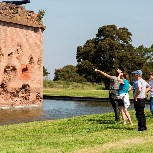 Park ranger, with a group of people, pointing at the historic fort wall. 
