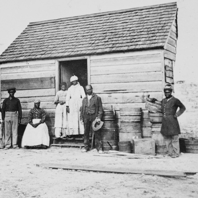 Black and white photograph of freedpeople in front of a house on Cockspur Island.