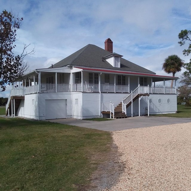 Exterior of white cottage house with wraparound porch during day