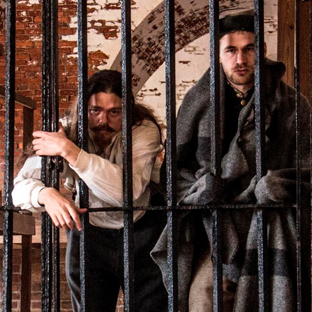Five male living historians dressed as confederate soldiers stand behind prison bars. 