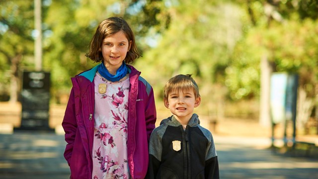 color photo of a young girl and boy standing outside