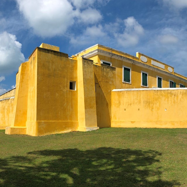 Bright yellow walls of a 19th century fort with a blue sky and ocean background