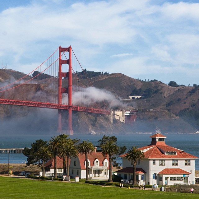 white military buildings with green lawns; golden gate bridge in the background