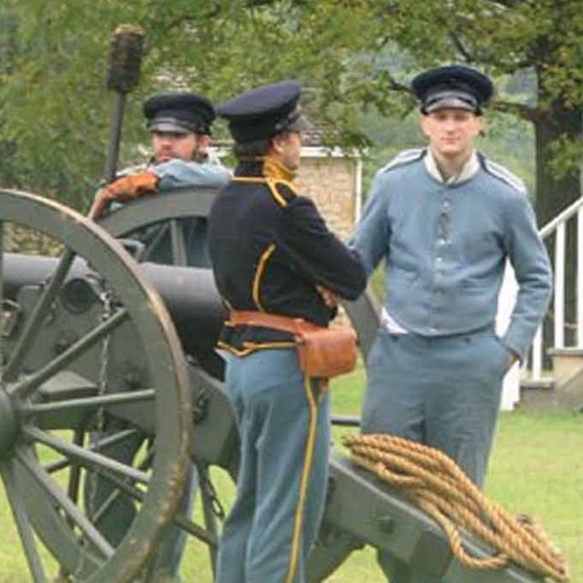 A group of artillery soldiers stand at a cannon preparing to fire