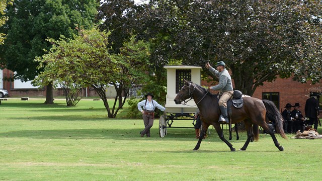 A Calvary reenactor with a sword raised in the air rides past and female deputy marshal and jail wag