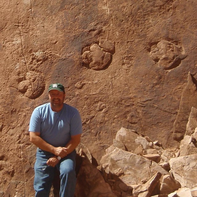 Photo of a person sitting by a large fossil trackway.