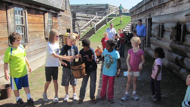 A row of children pass a wooden bucket to each other. 