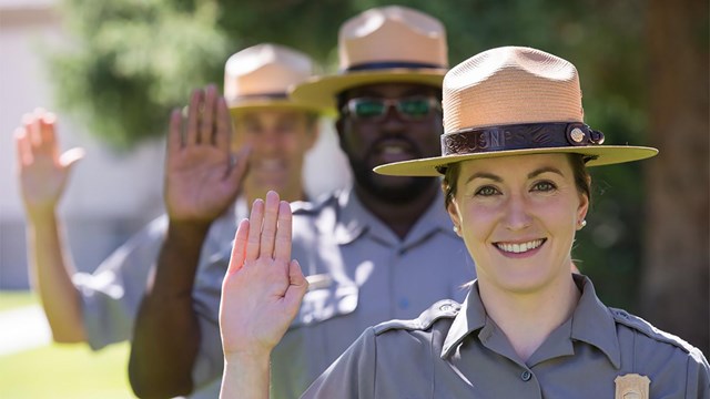 Several park rangers stand in a row holding up their right hand. 