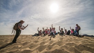 Students sit in front of a park ranger on a sand dune.