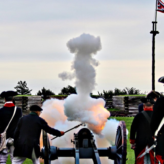 A cannon crew ignites the charge and smoke billows toward the fort wall. 