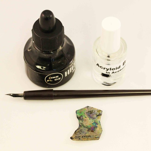 A fountain pen, ink well, and pottery sherds set neatly on a tablecloth. 