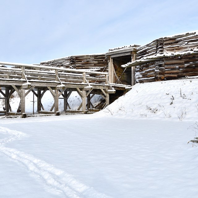 Looking from below at a snow-coated wooden bridge leading to the fort's walls.