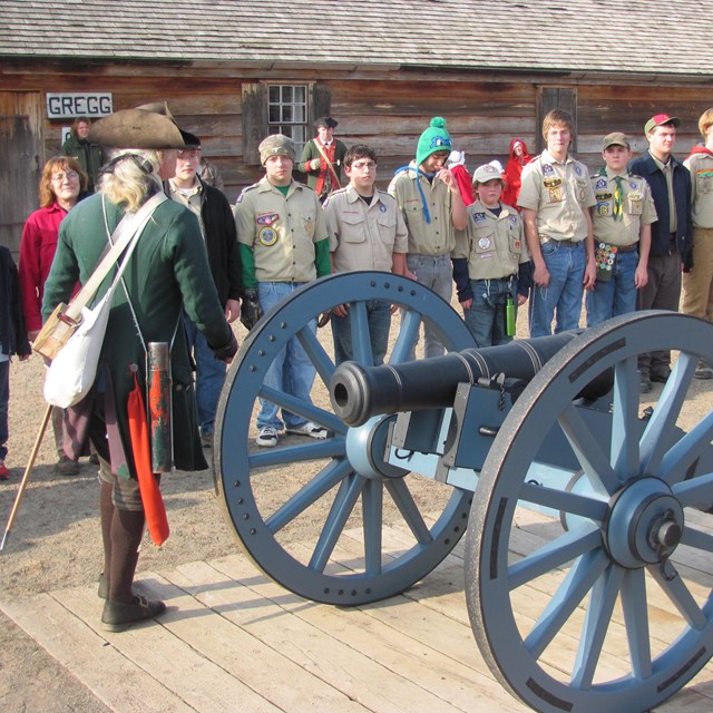 A cannon with a large groups of people standing at its side. 
