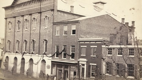 1865 black & white photo of Ford's Theatre and nearby buildings draped in mourning banners.