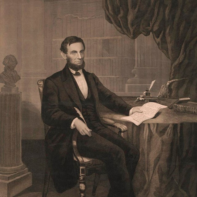 A man with a beard sits at a table, holding a quill pen in one hand and a paper in the other.