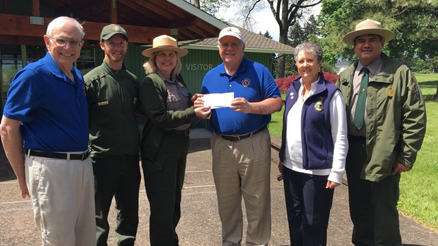 A group of people standing in front of the Visitor Center holding a check.