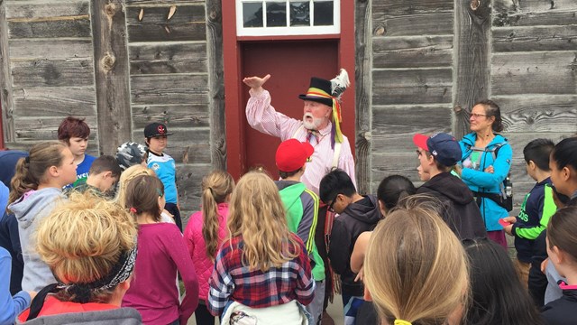 A man in a fur trader's costume talks to a school group inside Fort Vancouver.