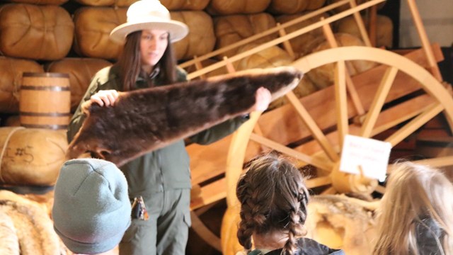 A park ranger holds up a fur for a group of children in the fort's fur store.