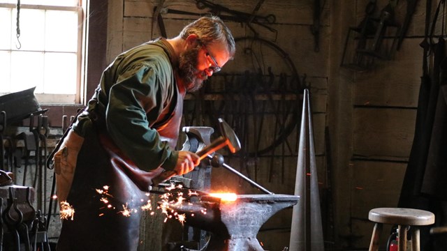 A blacksmith hammers a piece of metal on an anvil as sparks fly.