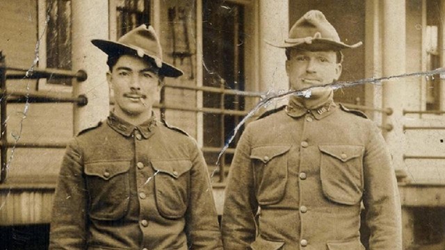 A black and white photo of two soldiers standing in front of a building at Vancouver Barracks.