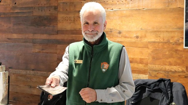 A volunteer dressed in grey and green handing out a Fort Vancouver brochure.