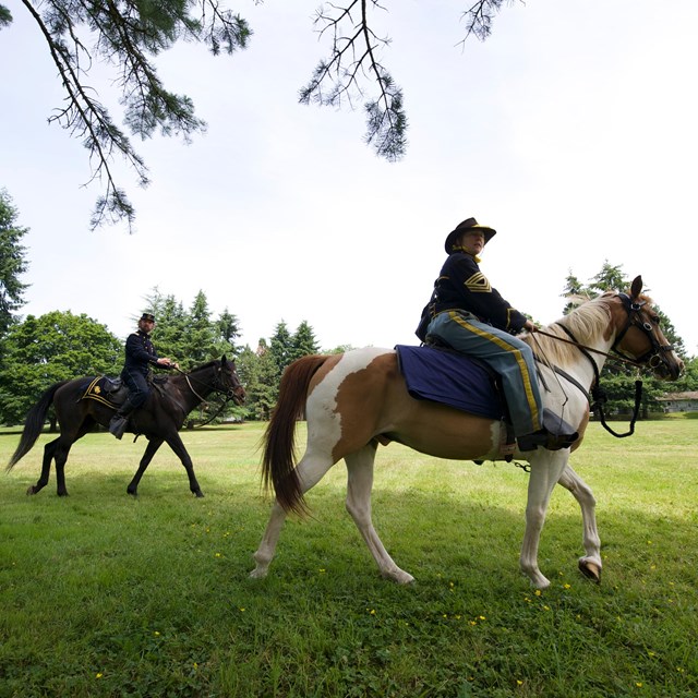 Costumed re-enactors dressed as 19th century US Army soldiers ride horses at Fort Vancouver NHS
