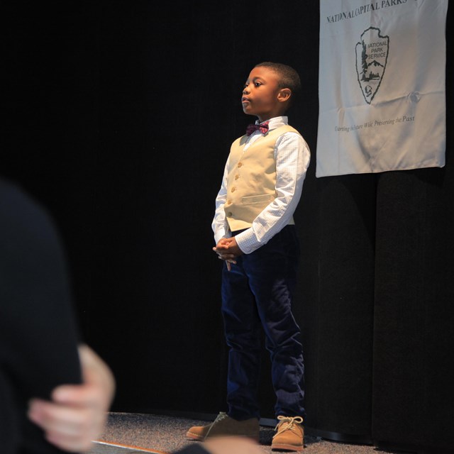 A young student gives a speech from a stage