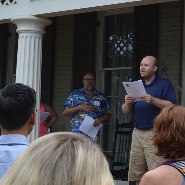 A man reads a speech from the front porch of a historic house