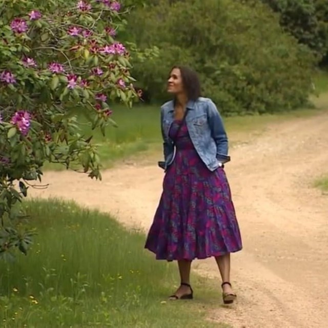 Woman walking on dirt road stopping to smell shrub
