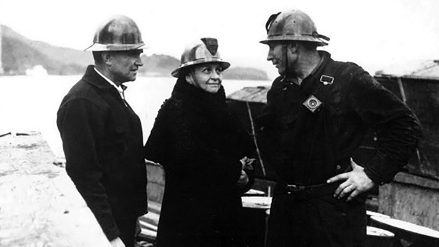 Francis Perkins stands between two men, all three wearing safety helmets.