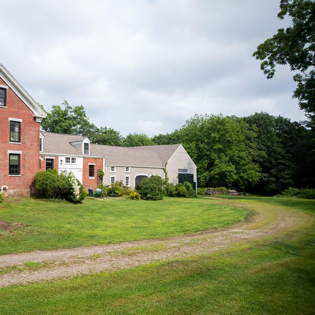 A gravel roadway bends towards the red brick and grey clapboard house.