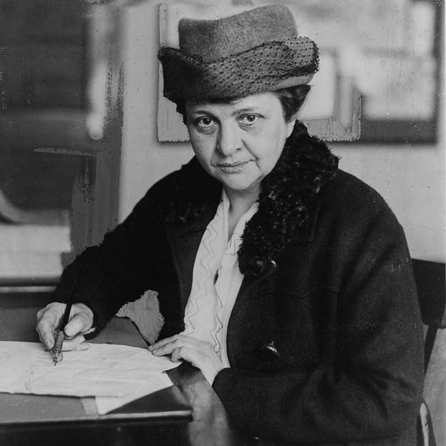 Francis Perkins seated at a desk, pen in right hand, looking directly at the camera.