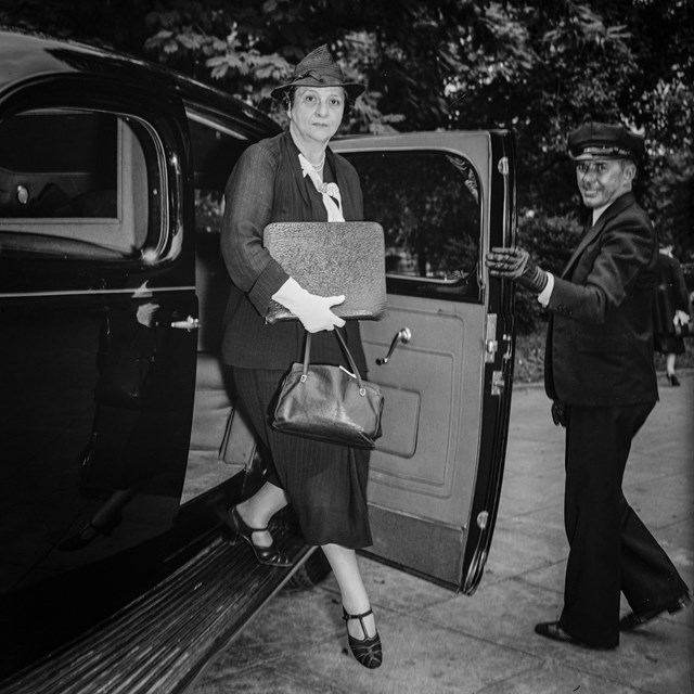 Francis Perkins stepping out of a car, a male driver holding the door open.
