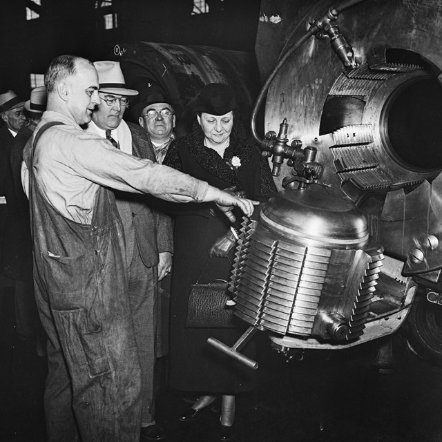 Francis Perkins and others shown heavy machinery equipment by a man in overalls.