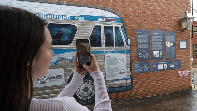 A visitor takes a picture of a painted bus mural and exhibits with her phone. 
