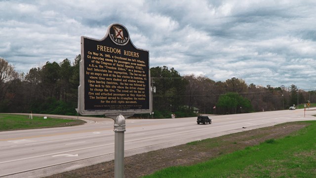 A Freedom Riders historical marker is in the foreground with a highway behind the sign. 