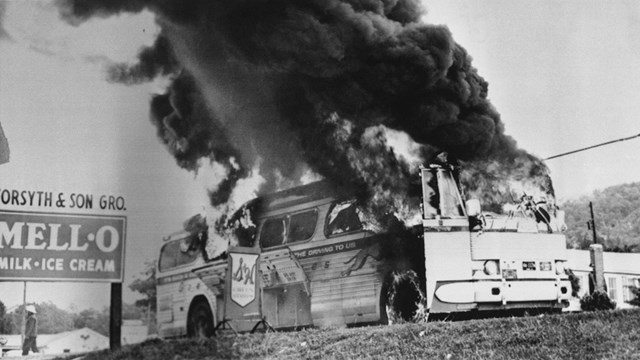 A bus burning with smoke pouring out of the door and windshield.